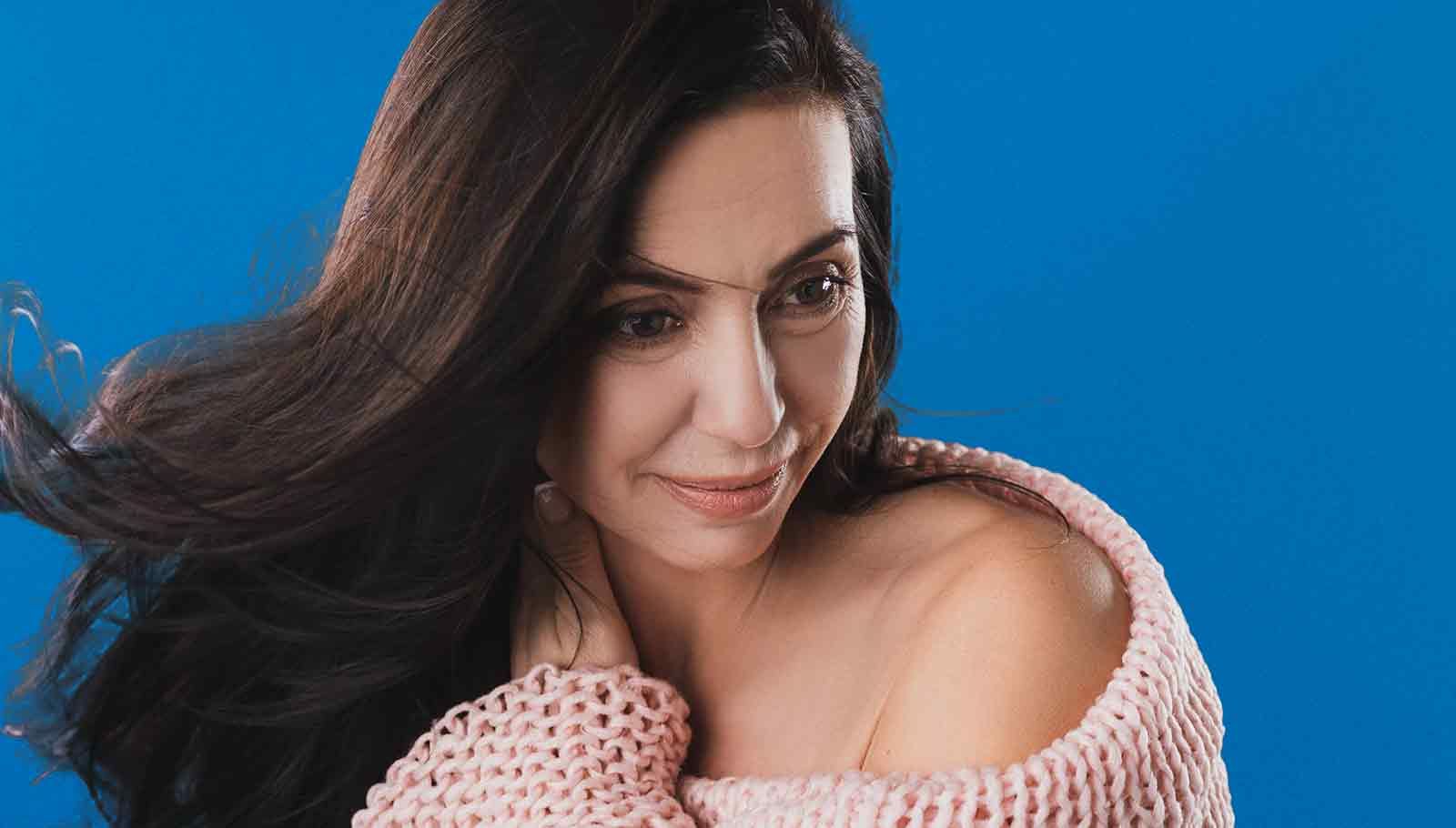 middle aged woman with dark long hair with her hand on her neck