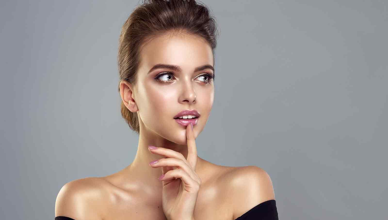 beautiful young woman with painted fingernail holding her hand up to her lips