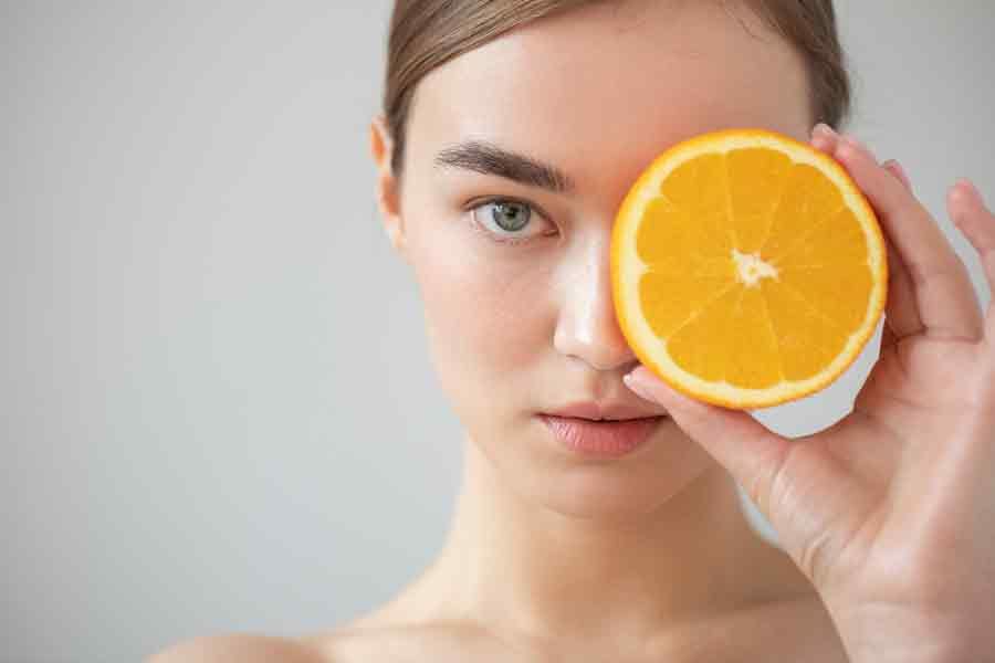 woman model holding a orange slice up to her left eye